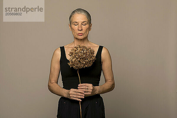 Gray haired woman holding withered hydrangea flower against brown background