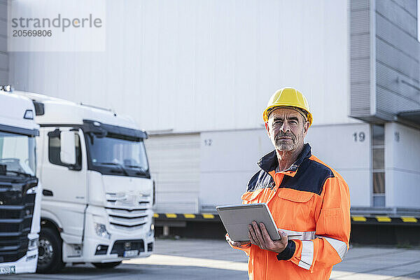 Confident mature foreperson wearing protective workwear standing with tablet PC at warehouse