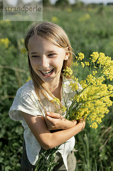 Cheerful girl holding bunch of flowers and standing in farm