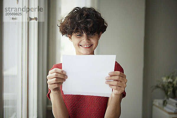 Happy young woman reading letter at home