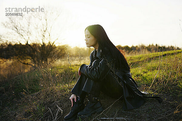 Young woman hugging knees in field on sunny day