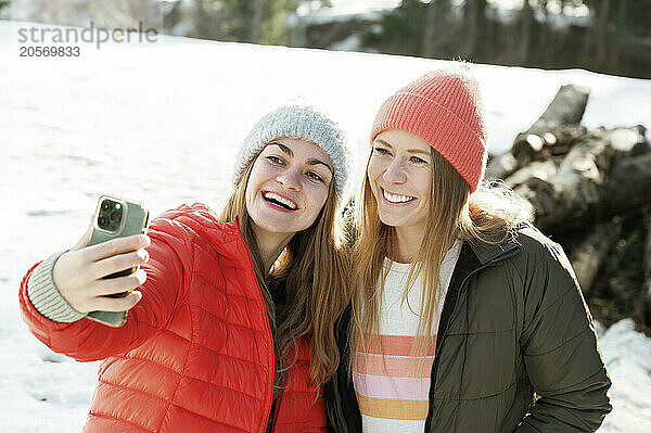 Happy friends in warm clothing taking selfie on snow field