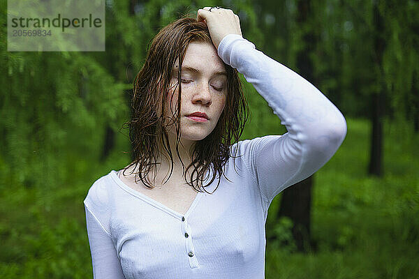 Woman with eyes closed and hand on head in rain