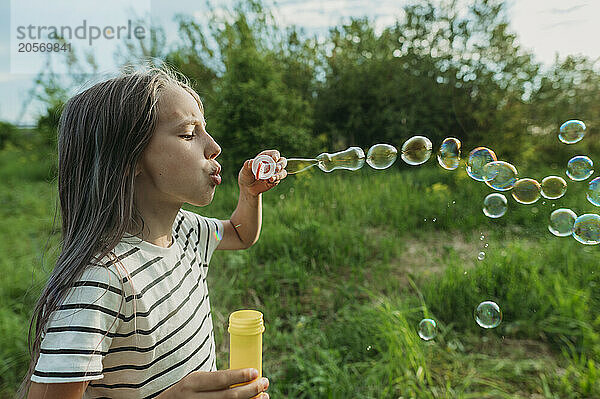 Girl blowing soap bubbles from bubble wand at back yard