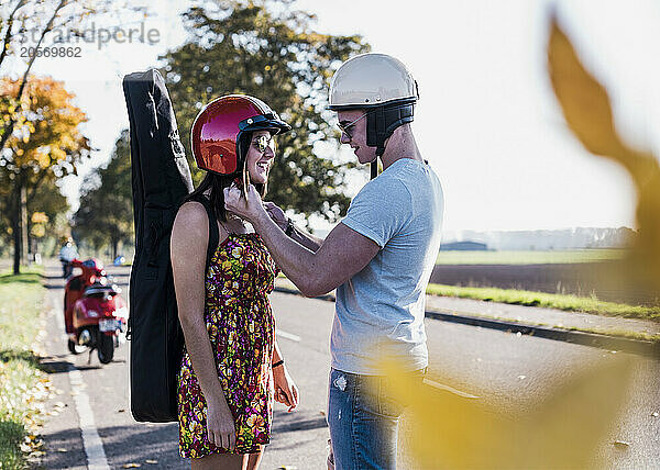 Young man helping girlfriend in wearing helmet at country road