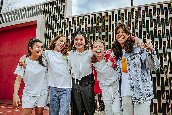 Happy teenage girls with arms around standing in front of wall at playground