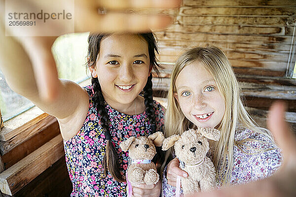 Smiling cute girls holding stuffed toys making frame with hands