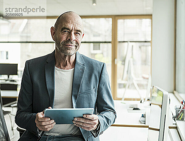 Confident mature businessman with tablet PC sitting at workplace