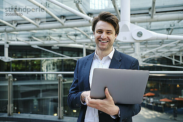 Smiling businessman standing with laptop