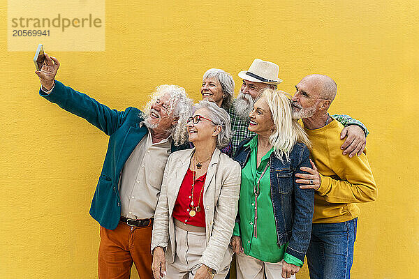 Happy senior man taking selfie with friends in front of yellow wall