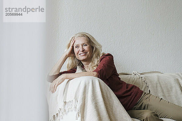 Happy blond senior woman relaxing on sofa in living room at home