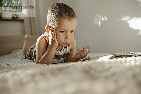 Cute boy on bed reading picture book in bedroom