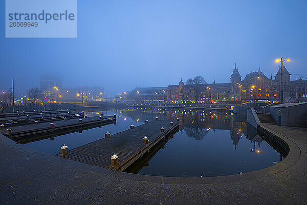 Amsterdam Railway Central Station and Basilica of St. Nicholas near Amstel river at blue hour