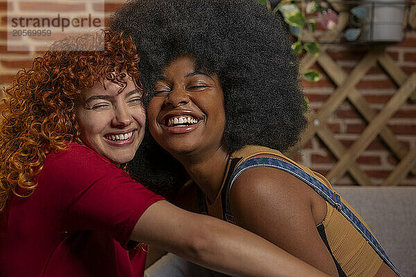 Smiling redhead woman spending leisure time with Afro roommate at home