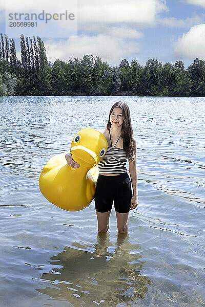 Happy girl holding rubber duck and standing in lake on sunny day