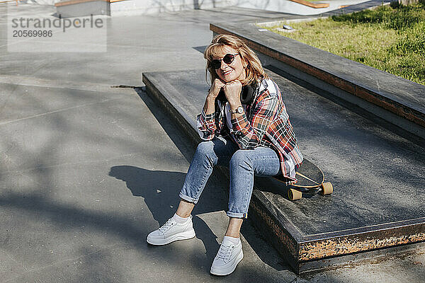 Senior woman leaning on elbow and sitting on skateboard in park