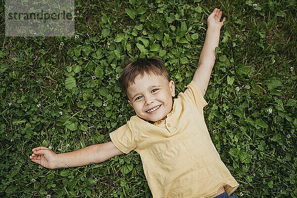 Cute boy with arms outstretched lying down on grass