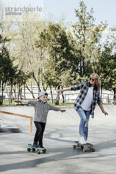 Happy grandmother and grandson skateboarding on sports ramp in park