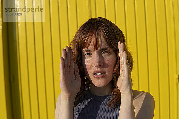 Confident redhead woman in front of yellow wall on sunny day