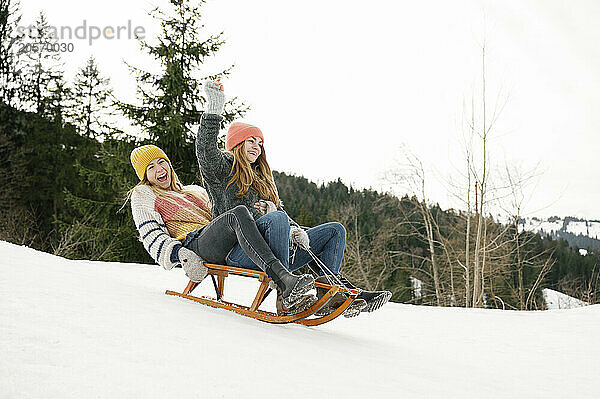 Playful friends sledding on snow covered hill