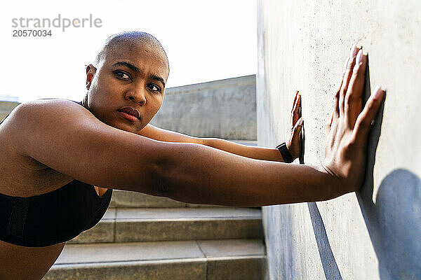 Bald woman doing wall push-ups on sunny day