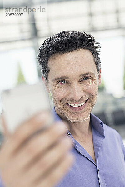 Happy handsome mature businessman using smart phone in airport