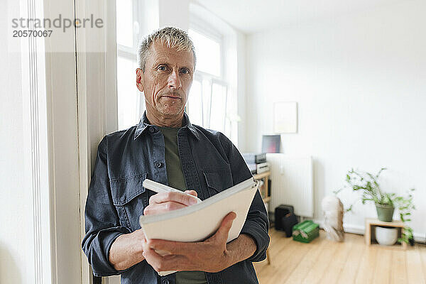 Confident senior man writing in diary leaning at home