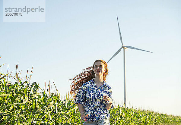 Teenage girl with red hair running in a green field with wind generators in the horizon