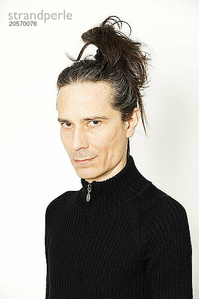 Smiling man with ponytail standing against white background