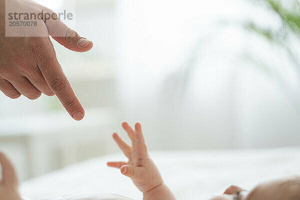 Hand of baby boy reaching for mother's finger at home