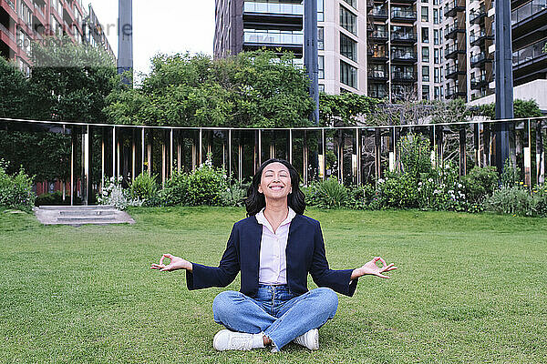 Smiling businesswoman practicing lotus position sitting at office park