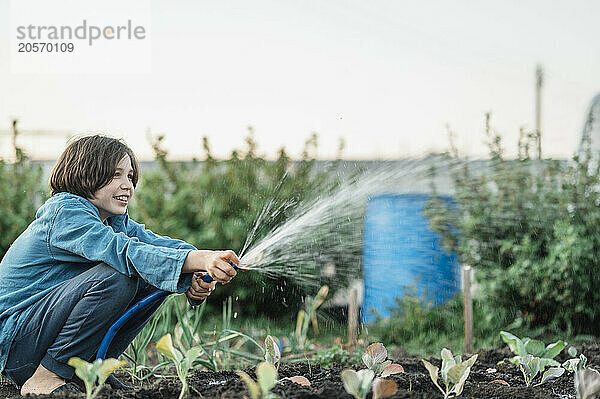 Happy boy watering plants in vegetable garden