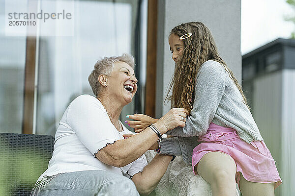 Happy grandmother spending leisure time with granddaughter outside house