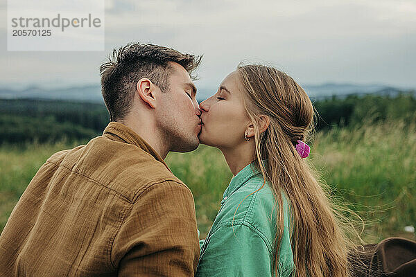 Boyfriend and girlfriend kissing at meadow on mountain