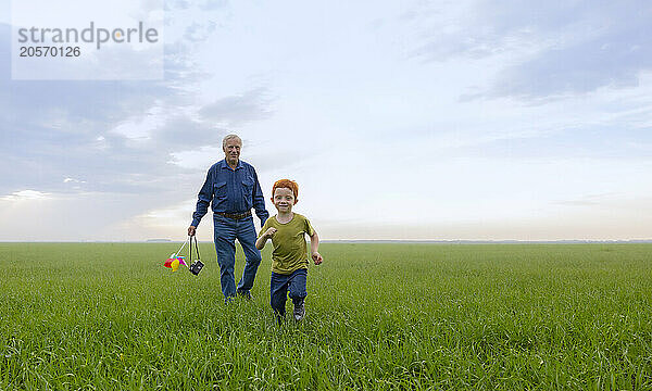 Senior man walking behind boy on grass under sky