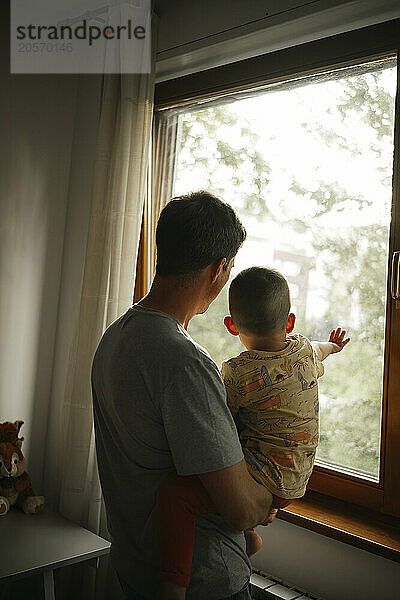 Father and son looking out through window from home