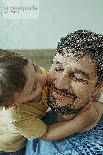 Boy kissing smiling father at home