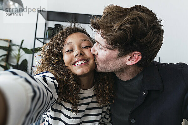 Doting father captures a sweet moment with his daughter as they take a selfie and share a loving kiss