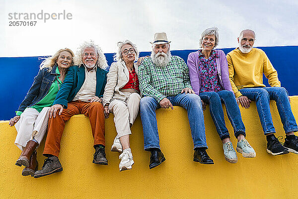 Happy senior friends sitting on yellow wall