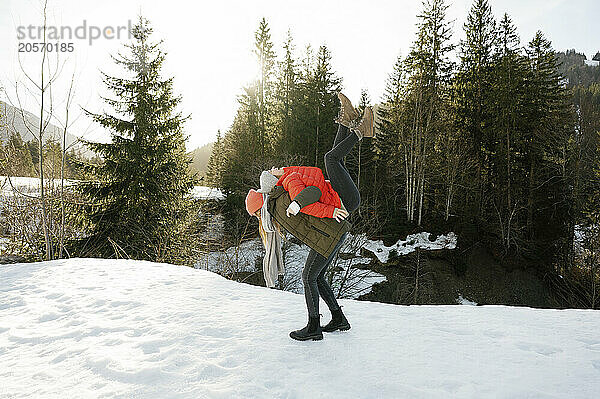 Carefree woman piggybacking friend on snow covered field