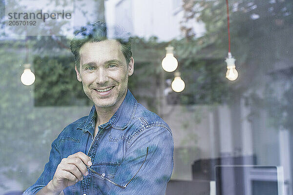 Smiling businessman with eyeglasses looking out through office window