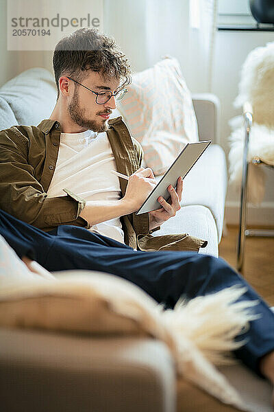 Young man using tablet PC reclining on sofa at home