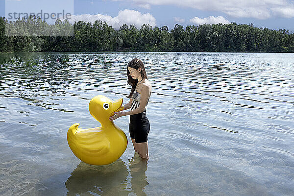 Girl looking at rubber duck and standing in lake under cloudy sky