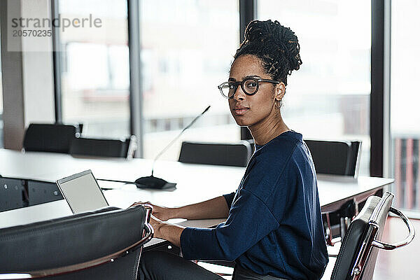 Confident young businesswoman wearing eyeglasses sitting with laptop at desk in office