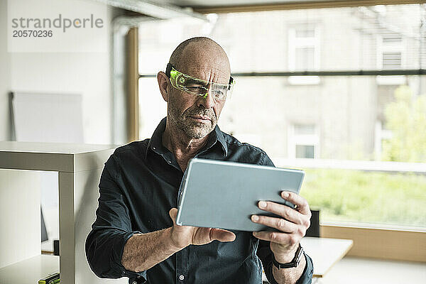 Confident mature businessman wearing smart glasses using tablet PC in office