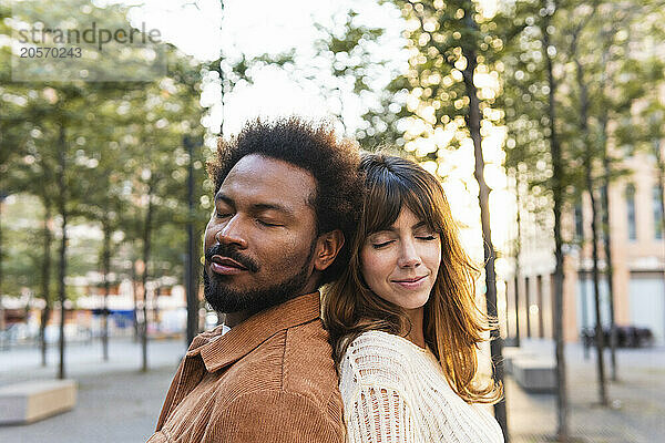 Multiracial couple standing back to back with eyes closed