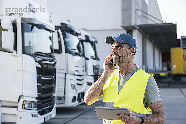 Confident manager talking on smart phone standing with tablet PC at warehouse