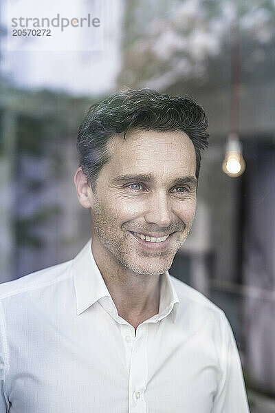 Smiling handsome businessman looking out through office window