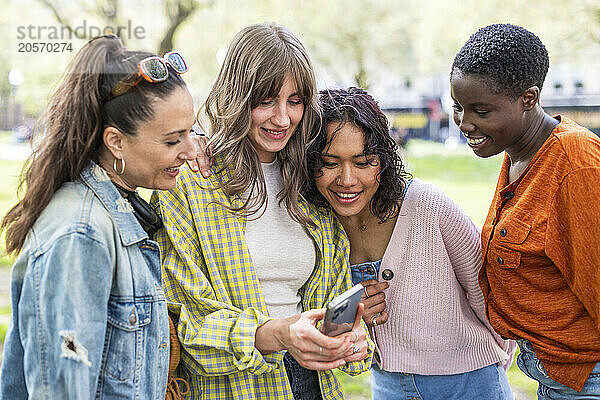 Young woman sharing mobile phone with friends at park