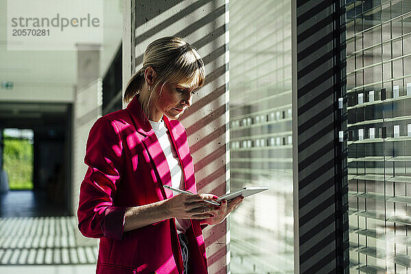 Blond businesswoman using tablet PC standing by window at office